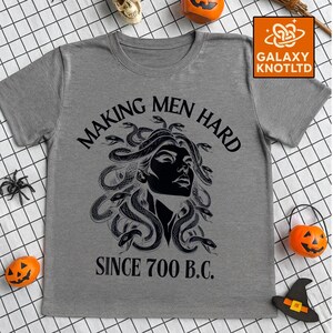 May include: Gray t-shirt with a black graphic of Medusa and the text "MAKING MEN HARD SINCE 700 B.C." The shirt has short sleeves and a crew neck. The Galaxy Knot Ltd. logo is in the upper right corner.