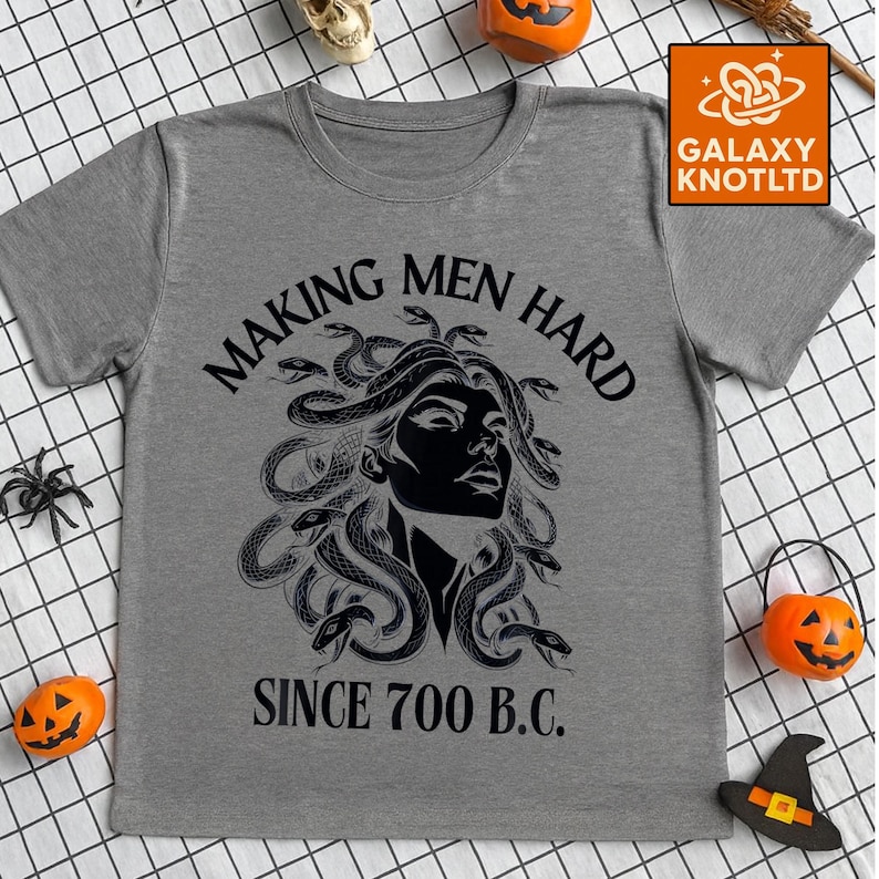 May include: Gray t-shirt with a black graphic of Medusa and the text "MAKING MEN HARD SINCE 700 B.C." The shirt has short sleeves and a crew neck. The Galaxy Knot Ltd. logo is in the upper right corner.