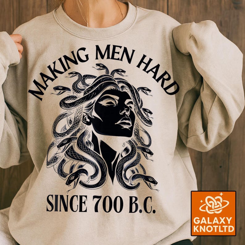 May include: A light beige sweatshirt with a black graphic of Medusa and snakes. The text "MAKING MEN HARD SINCE 700 B.C." is printed above and below the graphic. The Galaxy Knotltd logo is in the bottom right corner.