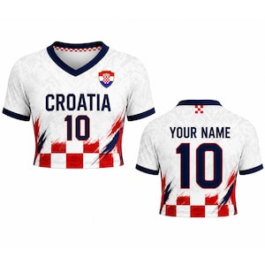 May include: White Croatia football shirt with red and blue details. The shirt displays the word "CROATIA" and the number "10" in navy blue. The front has a Croatian coat of arms. The back has the text "YOUR NAME" and the number "10".
