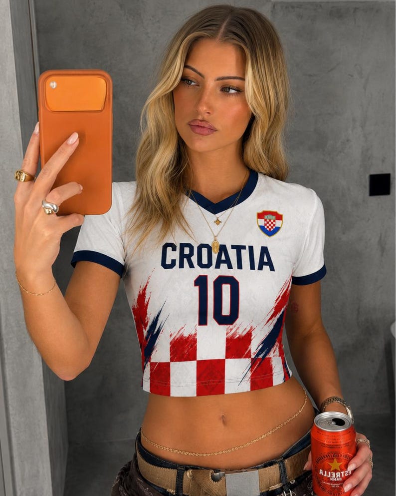 May include: White crop top with navy blue trim and the word "CROATIA" in navy blue. The number "10" is printed in navy blue. The top features a Croatian flag emblem and a red and white chequered pattern.