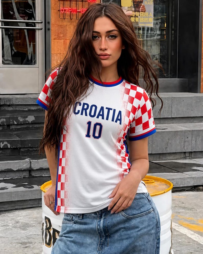 May include: White Croatia soccer jersey with red and white checkered pattern on the sleeves and shoulders. The jersey has blue trim and the word "CROATIA" and the number "10" in blue.