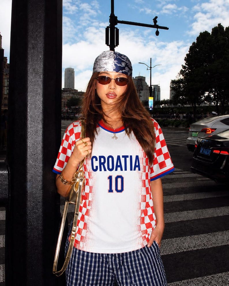 May include: A person wearing a Croatia soccer jersey with the word "CROATIA" and the number "10" in blue. The jersey has a red and white checkered pattern on the sleeves and shoulders. The person is also wearing a bandana, sunglasses, and striped pants.