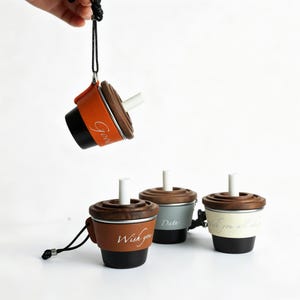 May include: Four miniature cup-shaped ornaments with black bases, brown wooden lids, and white straws. Each features a colored sleeve with white cursive text including Good, Wish you, Date, and Wish you all the best. One hangs from a black cord.