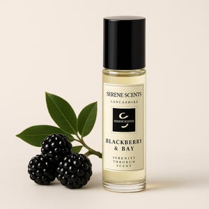 May include: A clear glass bottle with a black cap, labeled "Serene Scents Lancashire" and "Blackberry & Bay" scent. Beside it are three blackberries and green leaves, suggesting a natural fragrance.