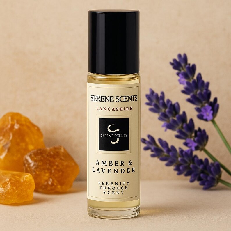 May include: A clear glass roll-on bottle with a black cap, labeled "Serene Scents Lancashire." The label reads "Amber & Lavender" and "Serenity Through Scent." Beside the bottle are sprigs of purple lavender and amber-colored crystals.