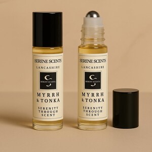 May include: Two glass roll-on perfume bottles with black caps, labeled "Serene Scents, Lancashire, Myrrh & Tonka, Serenity Through Scent." One bottle has a silver rollerball. The background is a solid beige color.