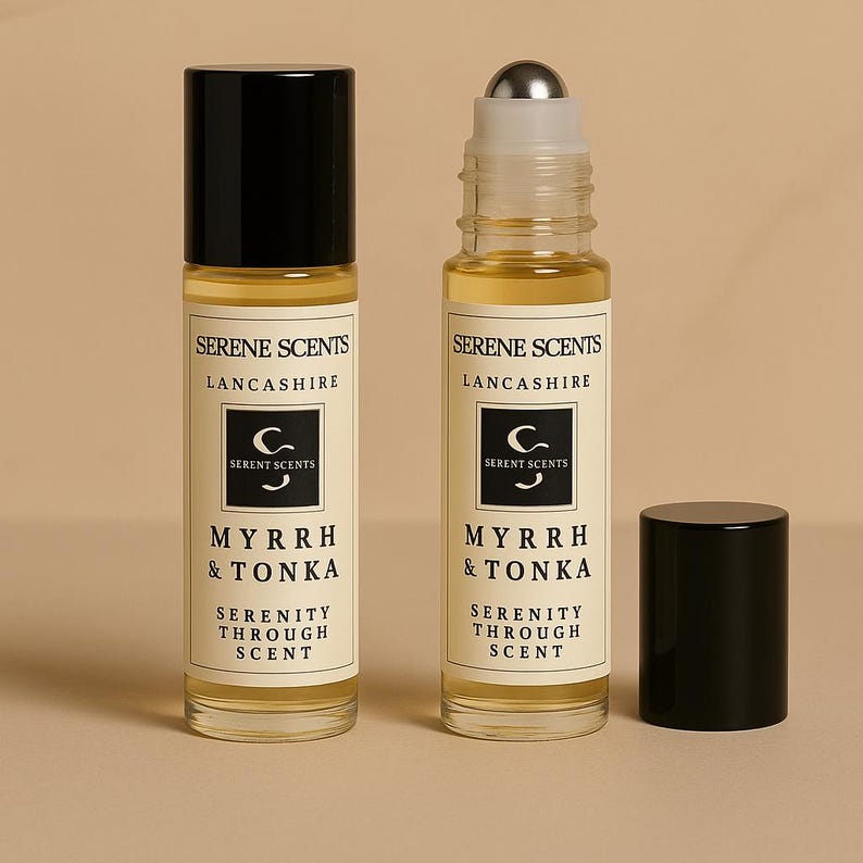 May include: Two glass roll-on perfume bottles with black caps, labeled "Serene Scents, Lancashire, Myrrh & Tonka, Serenity Through Scent." One bottle has a silver rollerball. The background is a solid beige color.