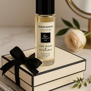 K&ouml;nnte beinhalten: Eine klare Glasflasche Serene Scents Lime Basil & Mandarin Duft, mit schwarzem Deckel, auf einer cremefarbenen Geschenkbox mit schwarzer Schleife. Das Etikett zeigt den Markennamen und die Duftbeschreibung. Die Flasche ist ca. 10 cm hoch.