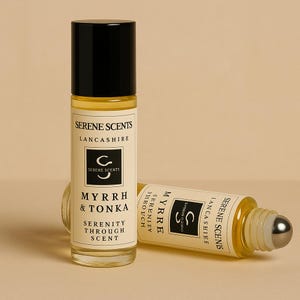 May include: Two glass roll-on perfume bottles with black caps. One is upright, the other is lying down. The labels read "Serene Scents Lancashire" and "Myrrh & Tonka Serenity Through Scent". The bottles have a silver rollerball.