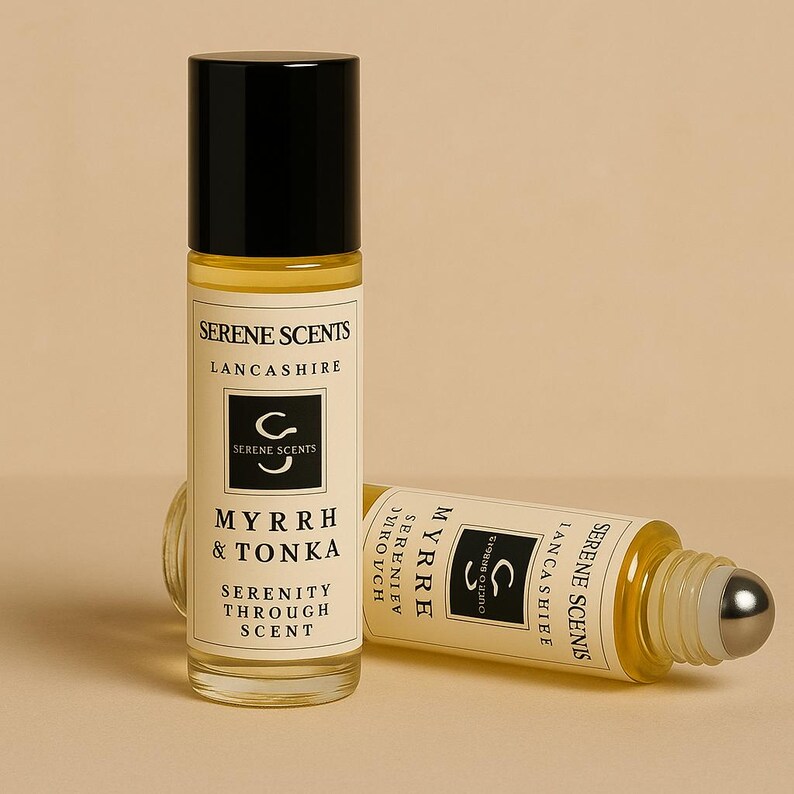 May include: Two glass roll-on perfume bottles with black caps. One is upright, the other is lying down. The labels read "Serene Scents Lancashire" and "Myrrh & Tonka Serenity Through Scent". The bottles have a silver rollerball.