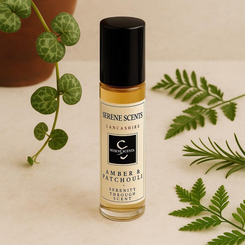 May include: A roll-on perfume bottle with a black cap and a clear glass body. The label reads "Serene Scents Lancashire" and "Amber & Patchouli". Green fern and vine leaves surround the bottle.