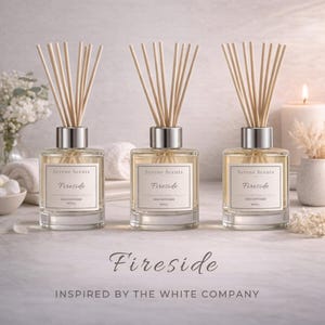 May include: Three glass reed diffusers with silver tops and wooden reeds. Each diffuser has a label that reads "Serene Scents Fireside". The text "Fireside" is also written in cursive at the bottom of the image. The image is inspired by The White Company.
