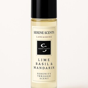K&ouml;nnte beinhalten: Eine transparente Glasflasche mit schwarzem Deckel, beschriftet mit "Serene Scents" und "Lime Basil & Mandarin". Das Etikett tr&auml;gt auch den Text "Serenity Through Scent". Die Flasche enth&auml;lt eine hellgelbe Fl&uuml;ssigkeit.