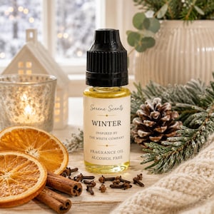 May include: A small clear glass bottle of fragrance oil with a black cap and a white label that reads Serene Scents WINTER INSPIRED BY THE WHITE COMPANY FRAGRANCE OIL ALCOHOL FREE. The bottle is surrounded by dried orange slices and cinnamon sticks.