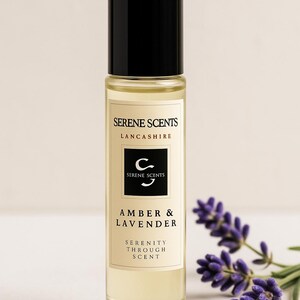 May include: A clear glass bottle of Amber & Lavender fragrance oil with a black cap. The label reads "Serene Scents, Lancashire" and "Serenity Through Scent." Sprigs of purple lavender are in the background.