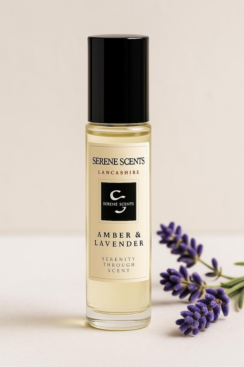 May include: A clear glass bottle of Amber & Lavender fragrance oil with a black cap. The label reads "Serene Scents, Lancashire" and "Serenity Through Scent." Sprigs of purple lavender are in the background.