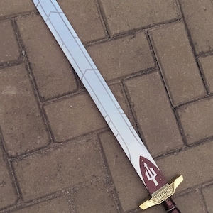 May include: A decorative sword with a silver blade and a brown and gold handle. The blade has a geometric design and a red trident symbol near the handle. The handle is brown with gold accents.