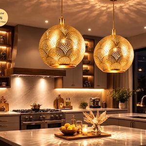May include: Two gold pendant lights with intricate cut-out patterns hang above a kitchen island. The kitchen features a stainless steel cooker, wooden cabinets, and a marble worktop. The image includes the text "Exclusive 20% Limited Time".