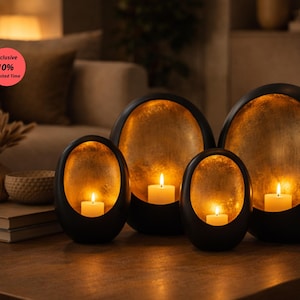 May include: A set of four black, oval-shaped candle holders with a gold interior. Each holder contains a lit, white candle. The candle holders are arranged on a wooden table, creating a warm, inviting ambiance. The image also includes a vase and a bowl.
