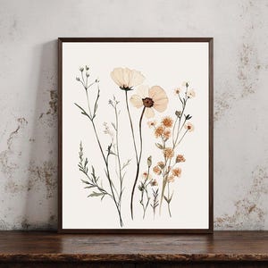 Könnte beinhalten: Ein gerahmter Aquarelldruck mit zarten botanischen Illustrationen. Das Kunstwerk zeigt eine Vielzahl von Wildblumen in sanften Pfirsich-, Creme- und Brauntönen vor einem weißen Hintergrund. Der dunkelbraune Rahmen verleiht dem Stück Wärme. Geeignet für Wohn- oder Schlafzimmer.