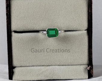 Puede incluir: Un anillo de plata con una gema verde rectangular con talla esmeralda, presentado en una caja de joyería negra con interior gris claro. La caja está sobre una superficie blanca, con el texto "Gauri Creations".