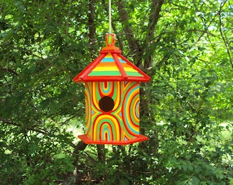 May include: A colorful birdhouse with a rainbow design and a red roof. The birdhouse is hanging from a tree branch.