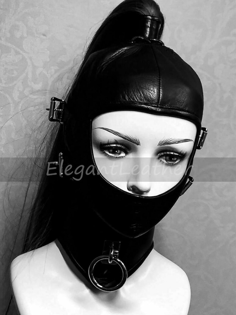 May include: Black leather hood with a face opening, secured with buckles and a neck collar with a metal ring. The text "ElegantLeather" is visible on the hood. The hood is designed to cover the head and neck.