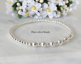 Könnte beinhalten: Ein kreisförmiges Armband aus kleinen, polierten Silberperlen mit einem Abschnitt aus größeren, runden Silberperlen. Der Text "Plain silver Beads" ist in der Mitte des Bildes aufgedruckt, umgeben von den Metallperlen in einer Schleife.