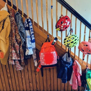 Peut inclure: Un escalier en bois avec divers articles suspendus à la rampe. On y trouve des vestes, des écharpes, des sacs à dos et des casques de différentes couleurs, comme le jaune, le rouge, le rose et le bleu. L'escalier a une finition en bois naturel.