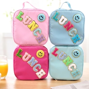 Peut inclure: Quatre sacs à déjeuner carrés en rose, bleu clair, magenta et vert menthe. Chaque sac dispose d'une poignée supérieure, d'une fermeture éclair et de patchs texturés, duveteux et colorés épelant le mot LUNCH, avec un écusson smiley circulaire.