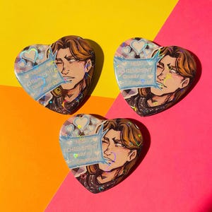 以下が含まれることがあります： 茶色の髪の人物のアニメ風イラストが描かれたハート型のピンバッジ3個。各バッジには「NEW ACHIEVEMENT Daddy's Favorite」と書かれた青いテキストボックスがあり、ホログラム仕上げでハートのアクセントが施されています。
