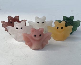 Puede incluir: Seis pequeñas figuras de murciélagos tallados en varios colores. Los murciélagos son de color rosa, blanco, amarillo, verde y marrón. Cada murciélago tiene pequeños ojos negros y alas extendidas.