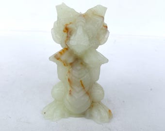May include: A carved figurine of a creature with a light green and brown color scheme. The figurine has a detailed design, with visible features such as a head, body, and legs. The material appears to be a type of stone or mineral.