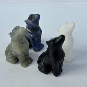 Puede incluir: Cuatro figuras de lobos talladas en piedra, en gris, azul, negro y blanco. Cada lobo está sentado con la cabeza levantada. Las esculturas son detalladas y parecen hechas de piedra natural, mostrando diversas texturas.