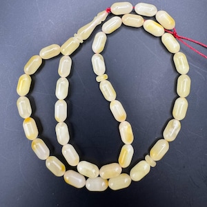 May include: A strand of prayer beads with oval-shaped, off-white beads. The beads have a slight yellow hue and are strung together with a red cord. The tassel and divider are also off-white.