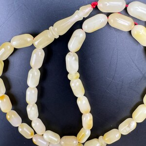 May include: A strand of prayer beads with oval-shaped, off-white beads. The beads are strung on a red cord, with a decorative, elongated bead at the top. The beads have a slightly translucent appearance.