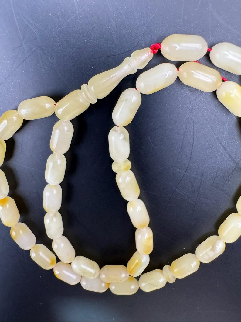 May include: A strand of prayer beads with oval-shaped, off-white beads. The beads are strung on a red cord, with a decorative, elongated bead at the top. The beads have a slightly translucent appearance.