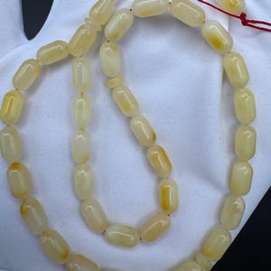 May include: A strand of prayer beads with oval-shaped, light yellow beads. The beads are strung on a red cord, with a decorative, elongated bead at the top. The beads have a smooth, polished appearance.