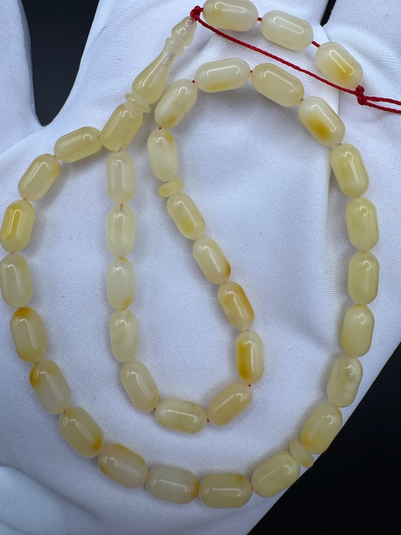 May include: A strand of prayer beads with oval-shaped, light yellow beads. The beads are strung on a red cord, with a decorative, elongated bead at the top. The beads have a smooth, polished appearance.