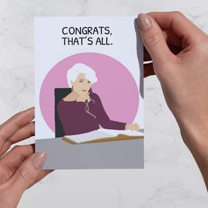 Könnte beinhalten: Glückwunschkarte mit dem Text "CONGRATS, THAT'S ALL." Die Karte zeigt eine Illustration einer Frau mit weißem Haar, die ein lila Oberteil trägt und an einem Schreibtisch sitzt. Ein rosa Kreis umrahmt die Frau. Die Karte wird von zwei Händen gehalten.