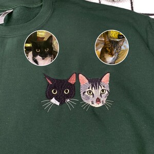 Custom embroidered forest green sweatshirt featuring two cat portraits, black and white tuxedo cat and gray tabby cat, personalized pet embroidery design, custom cat mom sweater, unique gift for cat lovers.