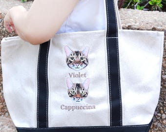 May include: Cream-colored tote bag with black trim and handles. The bag features embroidered cat faces, with the names "Violet" and "Cappuccina" below each cat. The bag is made of a sturdy canvas material.