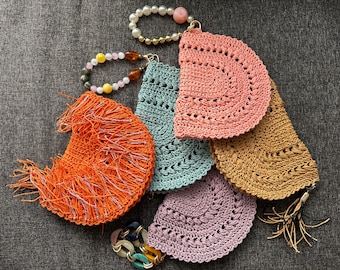 May include: A collection of handmade crochet items in various colors, including orange, teal, pink, and tan. The items appear to be small bags or pouches, some with fringe or tassels. Decorative beaded bracelets and necklaces are also present.
