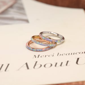 May include: Three thin rings stacked together, each featuring a band inlaid with iridescent, light blue opal-like material. The rings are crafted in different metal tones, including rose gold, yellow gold, and silver, resting on a cream-colored card.