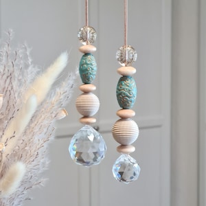 Könnte beinhalten: Zwei hängende Zierornamente. Jedes Ornament hat ein klares Kristallprisma, eine geriffelte Holzkugel, eine türkisfarbene Keramikperle und eine klare Glasperle. Aufgehängt an dünnen, hellbraunen Schnüren.