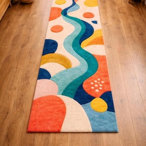 May include: A rectangular runner rug featuring a vibrant abstract pattern of wavy blue and teal lines, interspersed with circular and organic shapes in shades of orange, yellow, pink, and cream, set against a textured, multi-coloured surface.