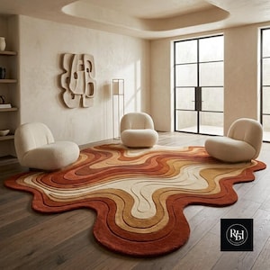 May include: A large, irregular, wavy-shaped area rug featuring concentric layers of warm colors including cream, tan, orange, and deep rust. Three cream-colored, rounded, low-profile armchairs are positioned on the rug in a room.