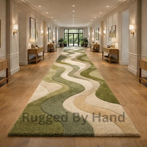 Pode incluir: Um tapete longo com padrão ondulado em tons de verde, bege e creme domina um corredor com piso de madeira. O design do tapete cria uma sensação fluida e orgânica. As palavras "Rugged By Hand" são visíveis.