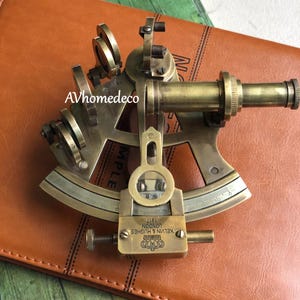 Op de afbeelding: Een vintage messing sextant, een navigatie-instrument met ingewikkelde details. De sextant heeft een telescoop, een gegradueerde boog en afstelknoppen. De tekst "KELVIN & HUGHES LONDON 1917" is zichtbaar. Geplaatst op een bruin lederen oppervlak.